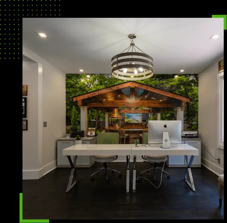 A modern home office with a white desk, two chairs, an iMac, a greenery gazebo mural on the back wall, ceiling light, and dark floors.