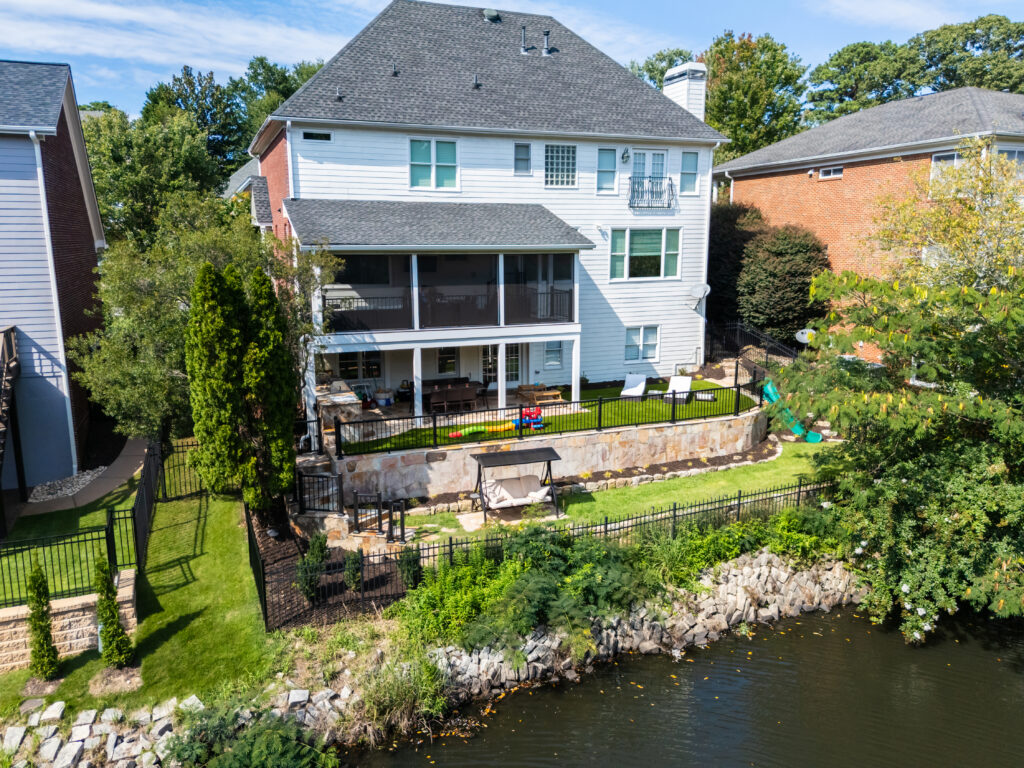 An elevated view shows a house with a screened porch, terraced lawn and planted retaining walls above the edge of a pond.