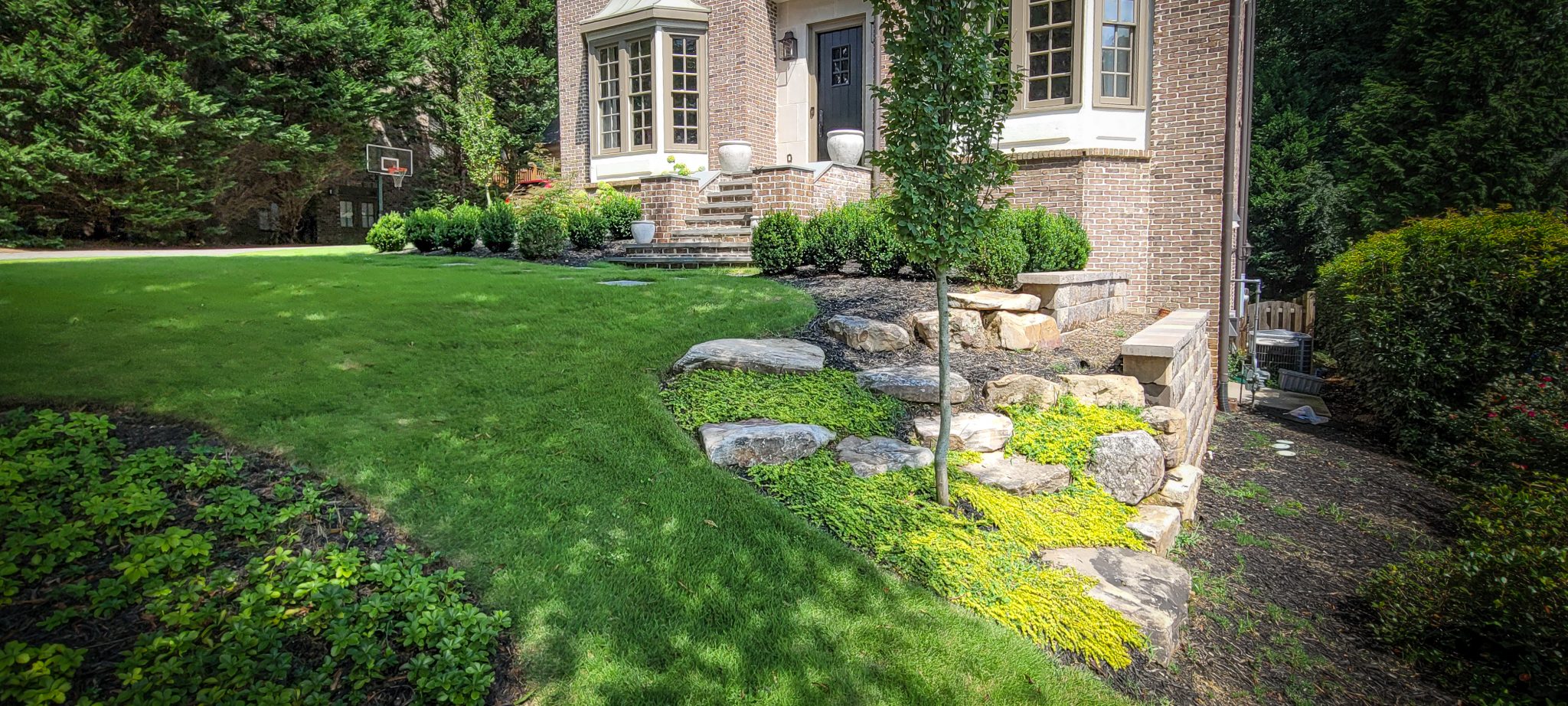 A brick house features a stone staircase and a front yard with a landscaped rock garden and a lawn.