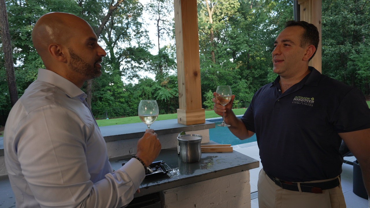 Two men toast with wine glasses at an outdoor kitchen counter in an Atlanta patio.